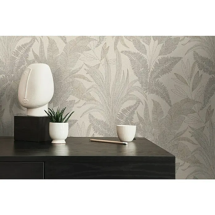 A.S. Création Stories of Life Vliestapete Dschungel - Beige-Gold, Floral, 10,05 x 0,53 m - Nahaufnahme eines dekorierten Tisches mit einer Skulptur, einer Pflanze und einem Bleistift vor einer botanischen Tapete.