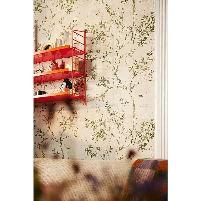 A.S. Création Stories of Life Vliestapete Zweig - Beige-Grün-Gold, Floral, 10,05 x 0,53 m - Roter String-Wandregal mit dekorativen Elementen vor einer Wand mit floralem Muster. Das Regal bietet Stauraum und verleiht dem Raum eine persönliche Note.