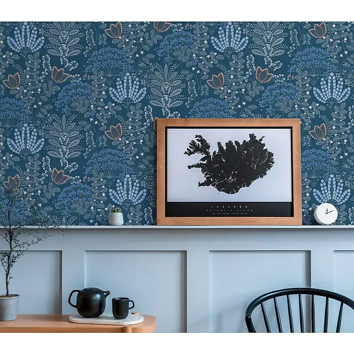 A.S. Création Famous Garden Vliestapete - Blau-Weiß-Grau, Floral, 10,05 x 0,53 m - Dekoratives Interieur mit blauem floralem Hintergrund, einem gerahmten Island-Poster und stilvollen Wohnaccessoires auf einem Regal.