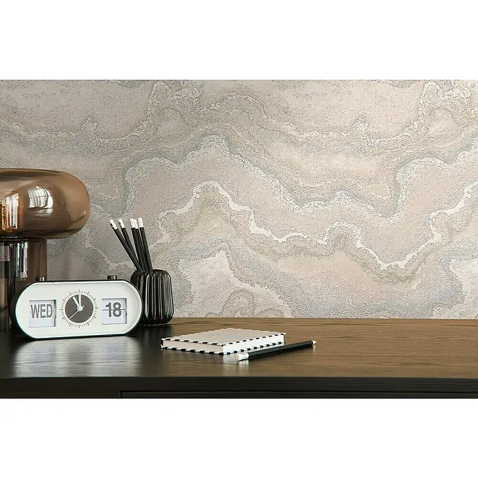 A.S. Création Stories of Life Vliestapete Marmoroptik Metallic-Effekt - Beige-Creme-Silber, Steinoptik, 10,05 x 0,53 m - Ein Flip-Kalender und ein Stifthalter auf einem Schreibtisch, ergänzt durch ein Notizbuch und einen Stift, vor einer strukturierten Wand.