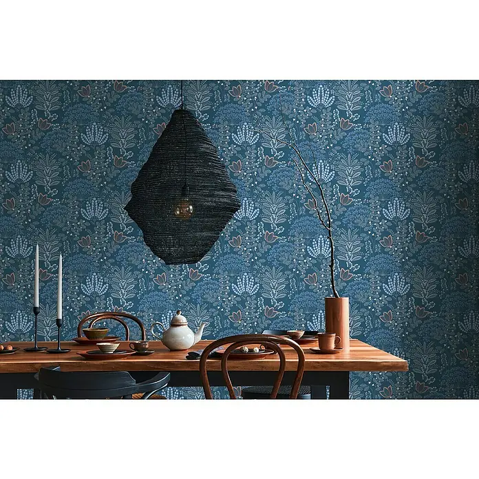 A.S. Création Famous Garden Vliestapete - Blau-Weiß-Grau, Floral, 10,05 x 0,53 m - Elegantes Esszimmer mit Holztisch, Geschirr und auffälliger Hängelampe vor floral gemusterter Tapete.