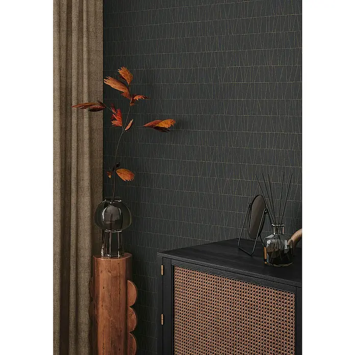 A.S. Création Jade 2 Vliestapete - Schwarz-Gold-Anthrazit, Grafisch, 10,05 x 0,53 m - Elegantes Interieur mit einer schwarzen Kommode, einem Holzhocker mit einer Glasvase und einer Wand mit einem geometrischen Muster.