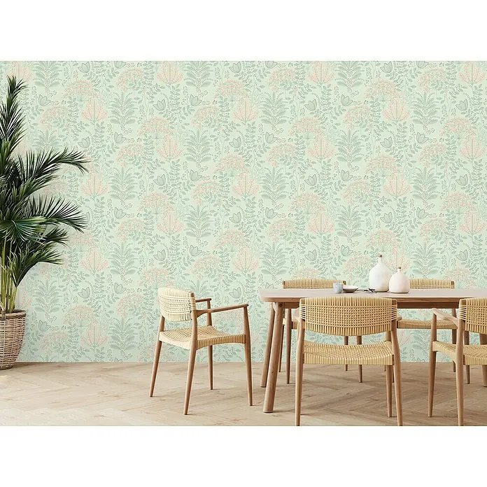 A.S. Création Famous Garden Vliestapete - Grün-Grau-Rosa, Floral, 10,05 x 0,53 m - Eine einladende Esszimmerszene mit einem Holztisch und Korbstühlen vor einer floral gemusterten Wand, die eine warme und stilvolle Atmosphäre schafft.