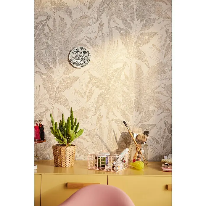 A.S. Création Stories of Life Vliestapete Dschungel - Beige-Gold, Floral, 10,05 x 0,53 m - Eine Nahaufnahme eines Schreibtisches mit einem Kaktus, einer Aufbewahrungsbox und Kunstbedarf, vor einer floralen Tapete.