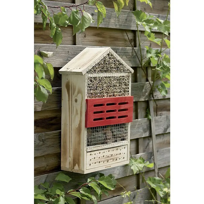 Windhager Insektenhotel - L x B x H: 33,5 x 14 x 49,5 cm, Holz, Naturbraun/Rot, Geflammt - Ein hölzernes Insektenhotel hängt an einem Zaun und bietet Unterschlupf für verschiedene Insektenarten, um die Artenvielfalt im Garten zu fördern.
