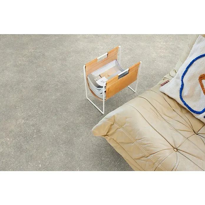 Beauflor PVC-Boden Meterware Tex-Style - 400 cm, Disa, Grau - Nahaufnahme eines Magazinständers aus hellem Leder mit weißem Metallgestell neben einem cremefarbenen Sessel mit Kissen.