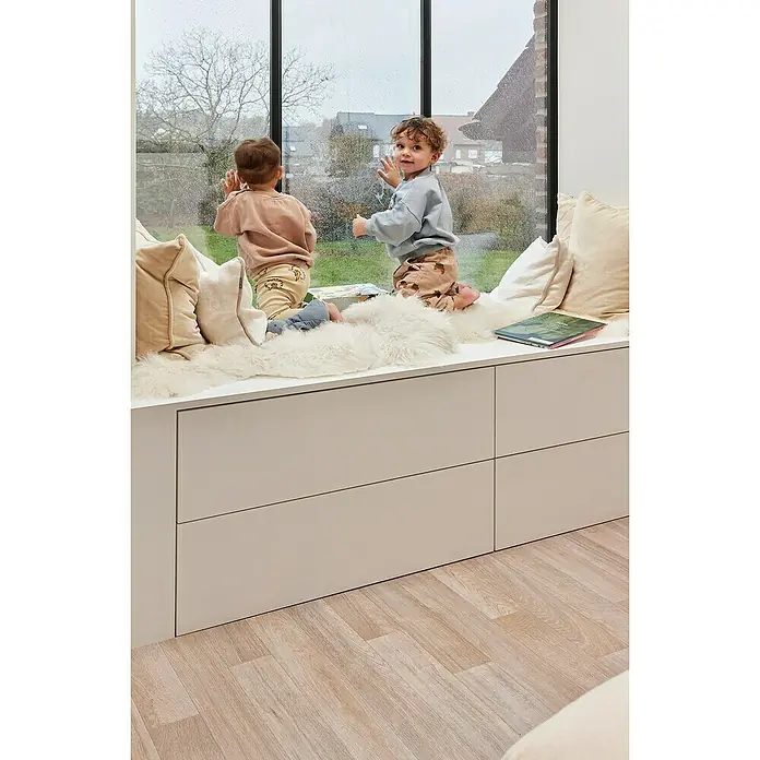 Beauflor PVC-Boden Meterware Atlantic - 400 cm, Natural Oak 949M, Braun - Kinder sitzen auf einer Fensterbank mit weißem Schrank. Die Bank ist mit Kissen und einem Fell bedeckt und bietet einen gemütlichen Platz zum Beobachten.