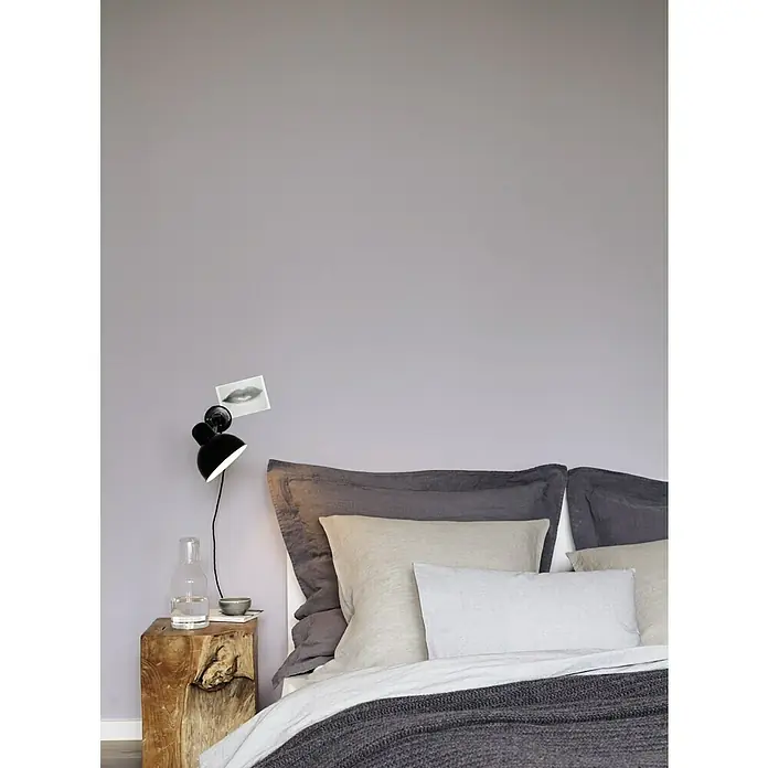Alpina Wandfarbe Feine Farben - Leiser Moment, Matt, 2,5 l, Konservierungsmittelfrei - Schlafzimmer mit Holzhocker-Nachttisch, Lampe, Wasserflasche und Kissen in verschiedenen Grau- und Beigetönen für ein gemütliches Ambiente.