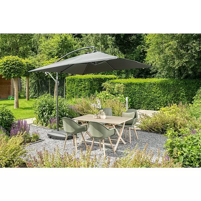 Garden Impressions Ampelschirm Corfu - Dunkelgrau, Bespannungsmaß (L x B): 250 x 250 cm - Outdoor-Essgruppe: Holztisch, vier grüne Stühle mit Holzbeinen und ein dunkelgrauer Freiarmschirm, auf einer Kiesterrasse im Garten.