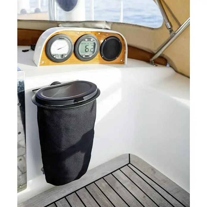 Yachticon Flextrash Wandhalterung Saugnapf - Passend für: Yachticon Mülleimer Flextrash, Klemmen - Eine schwarze Segeltuch-Abfalltasche mit einem schwarzen, abnehmbaren Deckel ist an einer weißen Wand neben dem Holzboden eines Bootes befestigt.