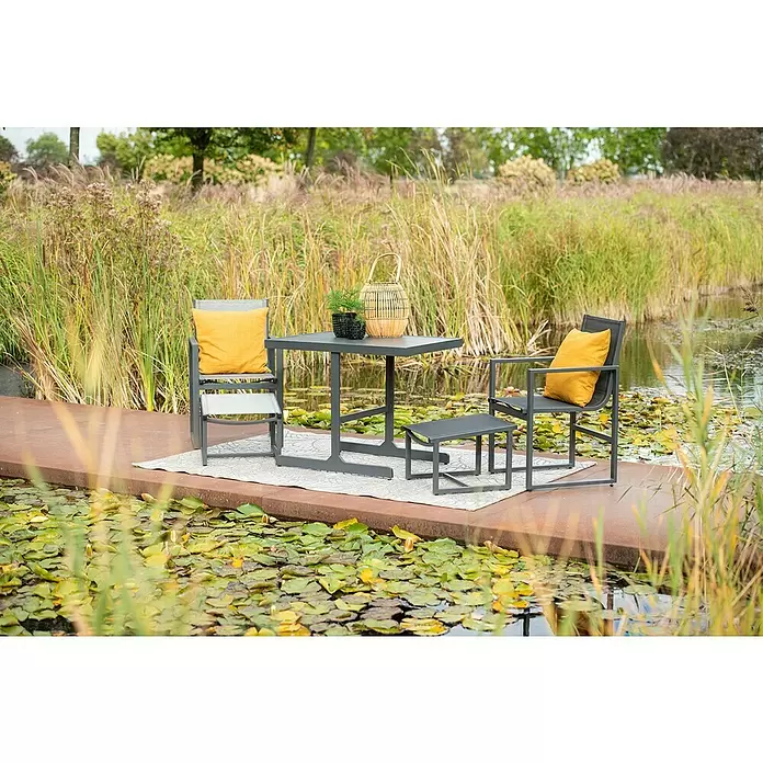 Garden Impressions Balkonmöbel-Set Alabama - 5 -tlg., Aluminium, Textilene, Schwarz/Anthrazit - Graues Outdoor-Loungeset mit gelben Kissen, auf einem Teppich neben einem Teich platziert, bestehend aus Tisch, Stühlen und Fußhocker.