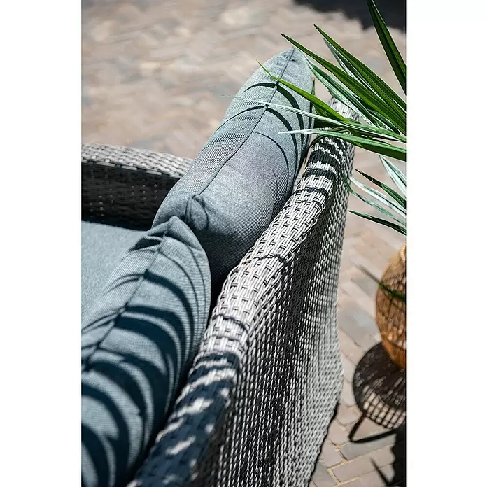 Garden Impressions Loungemöbel-Set Blue Bird - 4 -tlg., Aluminium, Polyester, Glas, Rechts, Grau - Nahaufnahme eines grauen Korbsessels mit passenden grauen Kissen, teilweise von grünen Blättern auf einer sonnigen Terrasse beschattet.
