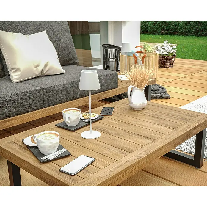 Starlux Paola Akku-Tischleuchte - 3 W, L x B x H: 11 x 11 x 36 cm, Weiß, Warmweiß - Ein stilvoller Couchtisch aus Holz mit Getränken, einem Smartphone und einer Lampe im Freien. Ideal für entspannte Stunden im Garten.