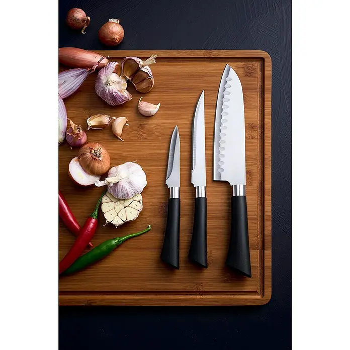 Set cuchillos de cocina - 3 pzs. - Una tabla de cortar de madera con tres cuchillos, cebollas, ajos y chiles.