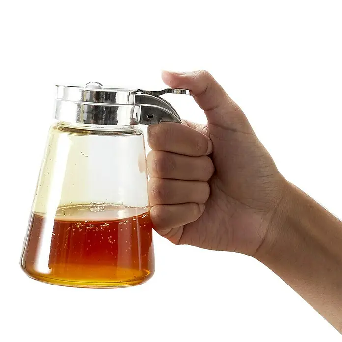 Frasco para miel - Vidrio - Primer plano de un dispensador de miel sostenido por una mano. El vidrio transparente muestra la miel dorada y burbujas.