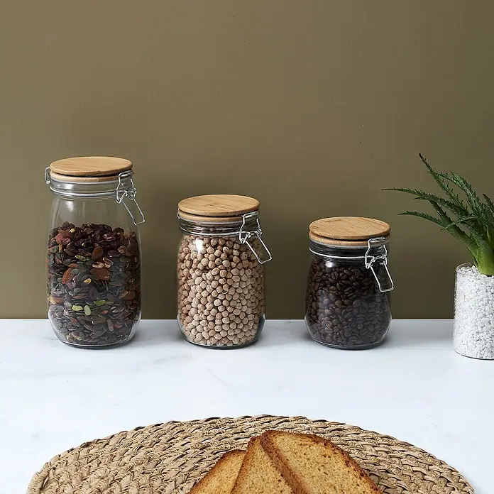 Frasco con cierre mecánico Bambú - 1,5 l, Vidrio, 1 pzs. - Frascos de almacenamiento de vidrio con tapas de madera llenos de semillas, garbanzos y granos de café, junto a tostadas y una planta.