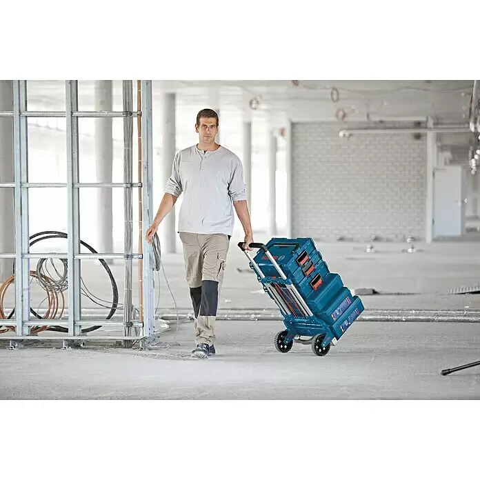 Bosch Professional Carretilla plegable Alu-Caddy - Específico para: Maletín de herramientas Bosch Professional L-BOXX, ABS - Hombre tirando de un sistema de apilamiento de herramientas Bosch azul en un carro en una obra.