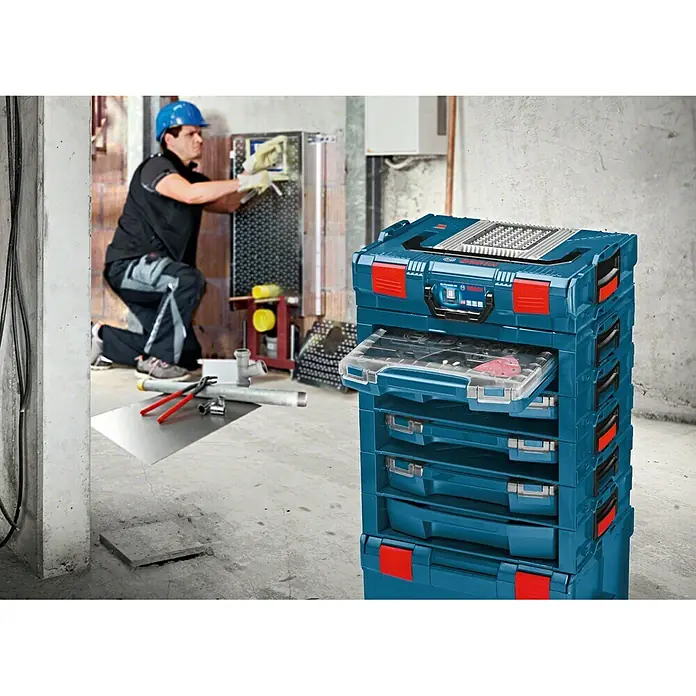 Bosch Professional Werkzeugkoffer i-Boxx 72 - L x B x H: 316 x 357 x 72 mm, ABS - Ein blauer Bosch Sortimo Werkzeugkoffer-Turm steht in einer Werkstatt, ein Arbeiter ist im Hintergrund sichtbar.