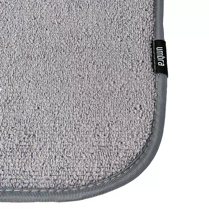 Umbra Abtropfmatte Udry - L x B x H: 61 mm x 46 cm x 4 cm, Kunststoff, Anthrazit - Ecke einer grauen, texturierten Stoffmatte mit eingefasstem Rand und schwarzem 'Umbra'-Etikett.