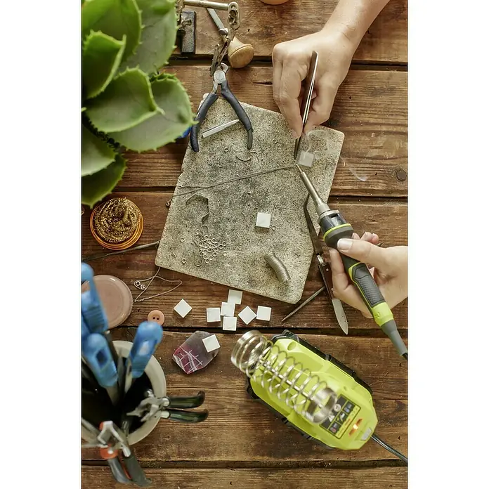 Ryobi ONE+ Soldador de puntos de batería R18SOI-0 - Apto para: Soldaduras finas - Primer plano de un artesano trabajando en joyas y un soldador sobre una mesa de madera.