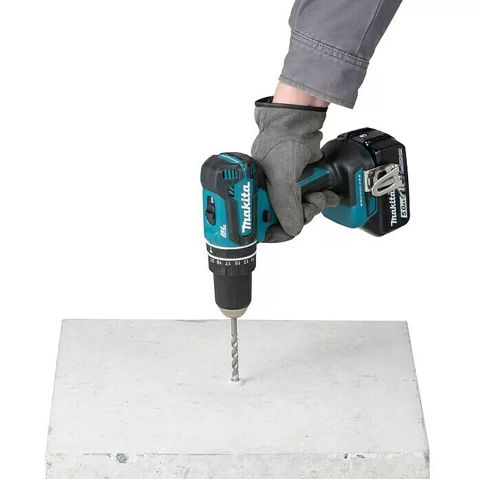 Makita LXT 18V Taladro atornillador percutor de batería DDF485RTJ - 18 V, 2 baterías, 5 Ah, 50 Nm - Taladro inalámbrico Makita sostenido por una mano enguantada, perforando hormigón.