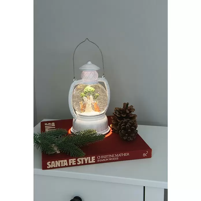 Konstsmide LED-Schneelaterne - Innen, 11,2 x 12,4 x 20 cm, Batteriebetrieben - Weißer Laternen-Schneeglobe mit beleuchteter Engelsfigur und Tannenzapfen, auf einem roten Buch dekoriert.