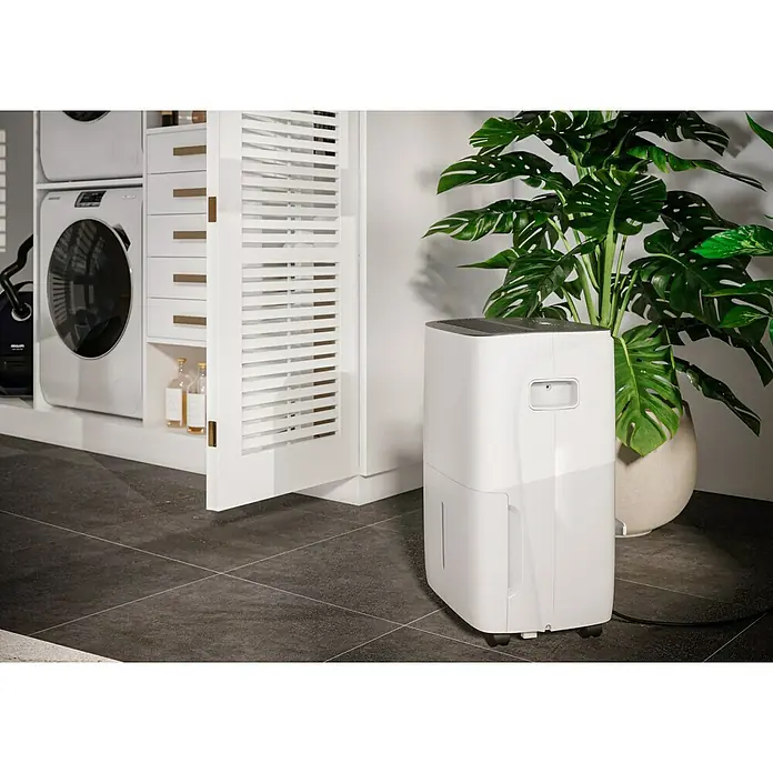 Voltomat Luftentfeuchter - Entfeuchtungsleistung: 60 l/Tag, Weiß/Grau, 900 W, Raumvolumen: 250 m³ - Ein Luftentfeuchter steht neben einem Schrank mit Wäschetrockner und einer Zimmerpflanze, um die Luftfeuchtigkeit zu regulieren und ein angenehmes Raumklima zu schaffen.