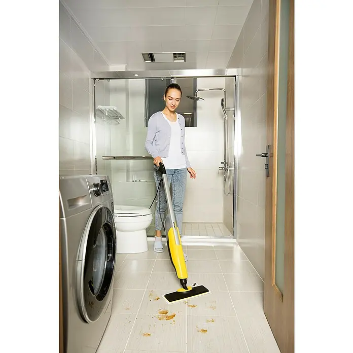 Kärcher Dampfreiniger SC 2 Upright EasyFix - 1.600 W, Aufheizzeit: 0,5 min, Behältervolumen: 0,4 l - Eine Frau reinigt mit einem gelben Kärcher Dampfreiniger den Boden in einem Badezimmer mit Fliesen.