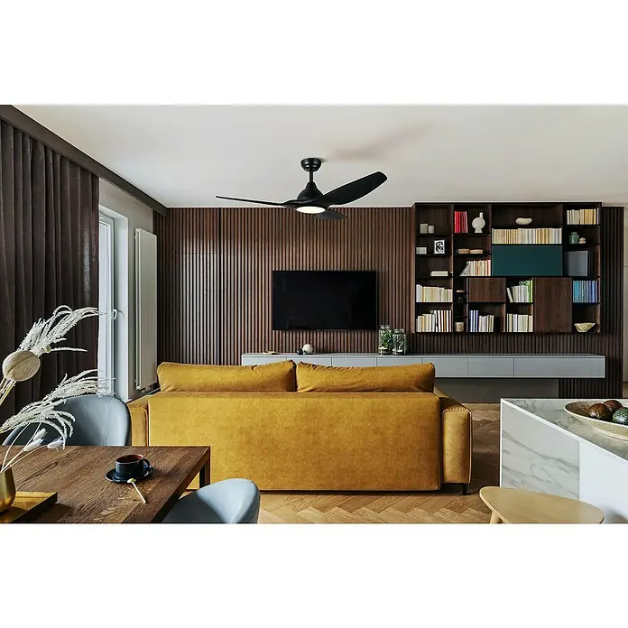 Deckenventilator mit LED-Beleuchtung Matteo - Schwarz-matt, 132 cm, 52 W - Wohnzimmer mit einem schwarzen Deckenventilator, einem ockerfarbenen Sofa und einem Fernseher an einer holzvertäfelten Wand.