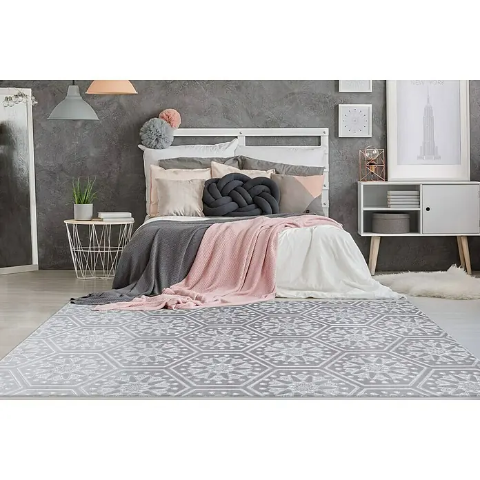 Kayoom Kurzflorteppich Monroe II - Grau/Blau, 230 x 160 cm, 100 % Polyester - Ein grauer Teppich mit geometrischen Mustern liegt in einem Schlafzimmer mit Bett und Nachttisch.