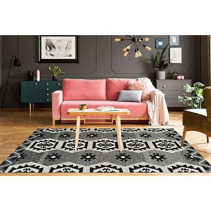 Kayoom Flachgewebeteppich Ethnie II - Grau, 230 x 160 cm, 100 % Baumwolle - Ein Wohnzimmer mit einem gemusterten Teppich, einem rosa Sofa und einem Holztisch. Der Teppich ist das Hauptprodukt im Raum.