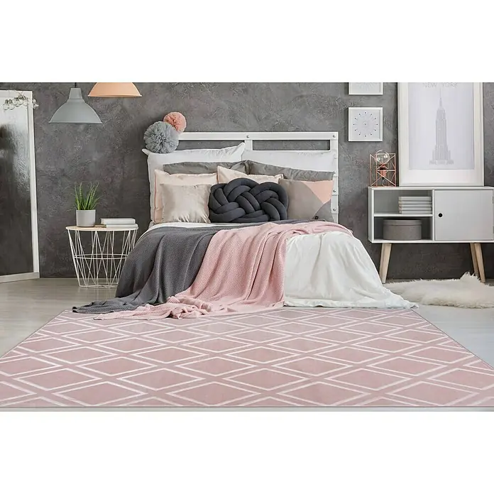 Kayoom Kurzflorteppich Monroe III - Rosa, 150 x 80 cm, 100 % Polyester - Ein rosa Teppich mit Rautenmuster liegt in einem Schlafzimmer mit einem Bett, Nachttisch und Kommode. Der Teppich verleiht dem Raum einen Hauch von Farbe.