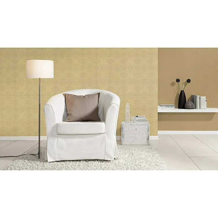 Rasch Berlin Vliestapete Muschel - Gold, Uni, 10,05 x 0,53 m - Einladender Wohnbereich mit einem weißen Sessel, einer Stehlampe und einem stilvollen Bücherregal, der eine gemütliche Atmosphäre ausstrahlt.