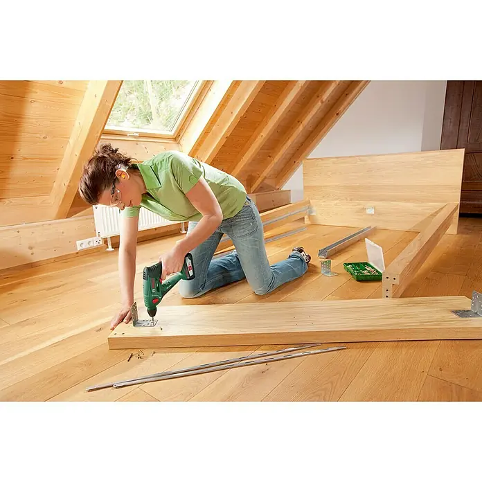 Bosch Power for All 18V Maschinenpaket -  - Frau montiert ein Holzbett mit einem grünen Bosch-Akkuschrauber. Verschiedene Werkzeuge und Teile liegen auf dem Boden.