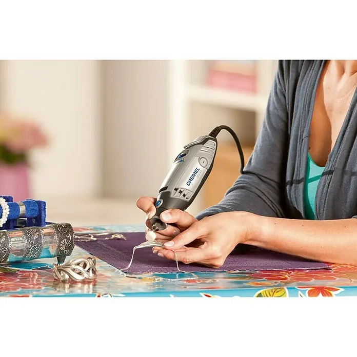 Dremel Multifunktionswerkzeug 3000-1/25 - 130 W - Eine Frau verwendet ein Dremel-Rotationswerkzeug für Schmuckarbeiten auf einem bunten Tisch. Präzise Bearbeitung mit dem Dremel-Werkzeug.