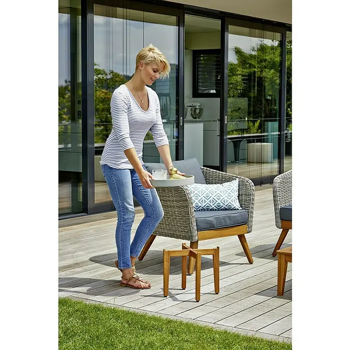 Sunfun Garten-Beistelltisch rund - Ø x H: 35 x 35 cm - Eine Frau stellt ein Tablett mit Getränken auf einen Beistelltisch aus Holz im Außenbereich, der zu einem Loungesessel gehört.