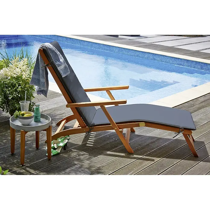 Sunfun Diana Gartenliege - B x T: 149 x 58 cm, Holz, Anthrazit/Braun, Rückenlehne verstellbar - Sonnenliege aus Holz mit grauer Auflage neben einem Beistelltisch mit Getränken und Obst am Pool.