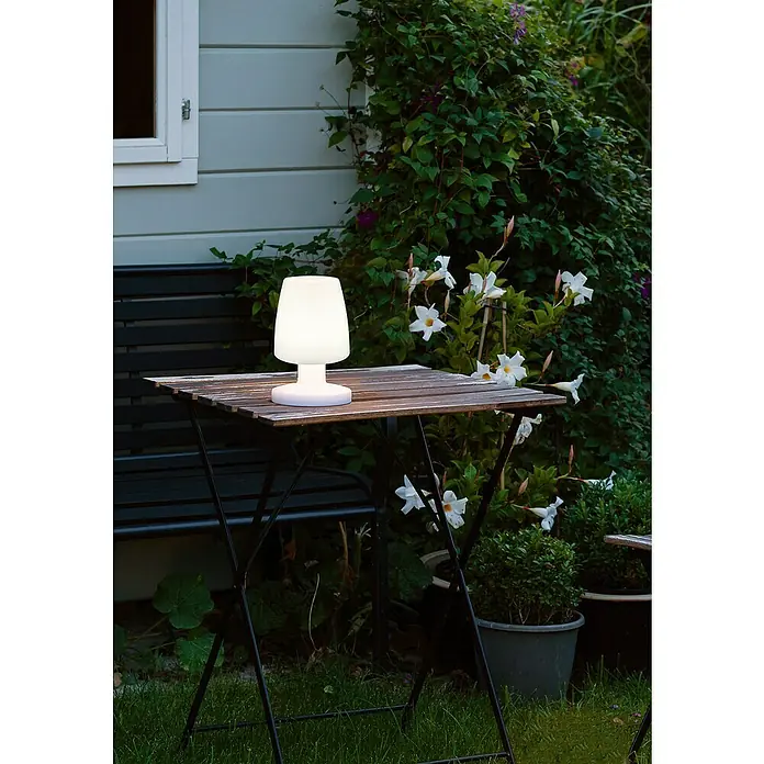 Reality Leuchten Akku-Tischleuchte Dora - 1,5 W, L x B x H: 13 x 13 x 21 cm, Weiß, Warmweiß - Eine moderne, kabellose Tischleuchte aus mattem Weiß mit sanftem Licht, ideal für gemütliche Abende im Freien auf einem Holztisch.
