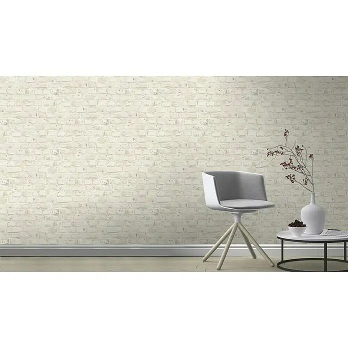 Rasch Vliestapete - Grau/Weiß, Steinoptik, 10,05 x 0,53 m - Wandbild mit einer weißen Backsteinmauer, einem modernen Stuhl und einem Beistelltisch mit Dekorationen für eine stilvolle Raumatmosphäre.