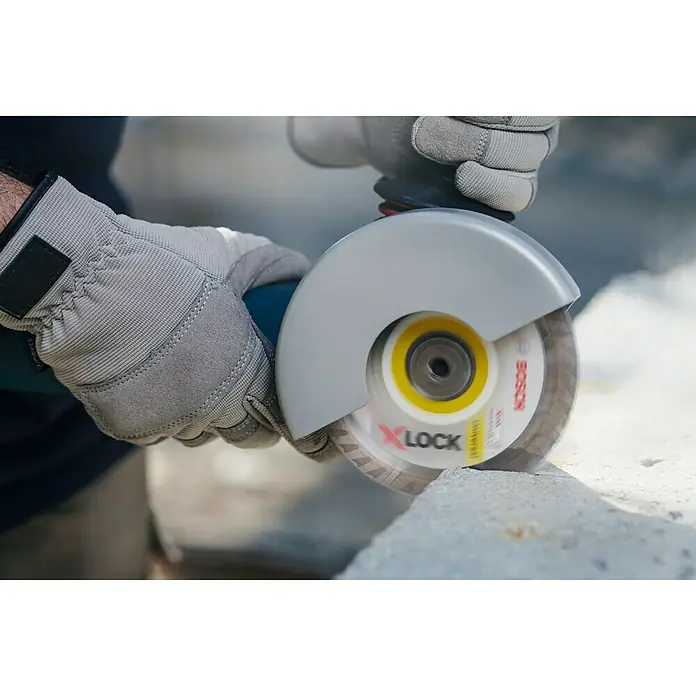 Bosch Professional X-Lock Disco de corte Standard - Ø x Es: 125 x 1 mm, Orificio: 22,23 mm - Primer plano de una amoladora angular Bosch X-LOCK cortando piedra, operada por una persona con guantes protectores.