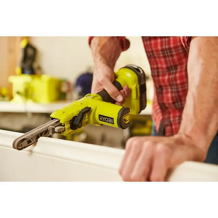 Ryobi ONE+ Maschinenpaket - Akku-Bandschleifer R18PF-0 + gratis Starter-Kit - Nahaufnahme eines gelben Ryobi-Bandschleifers beim Schleifen einer weißen Oberfläche, der für präzise Schleifarbeiten konzipiert ist.