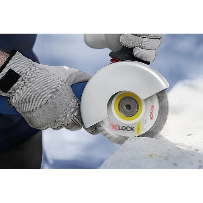 Bosch Professional X-Lock Elektro-Winkelschleifer GWX 14-125 - 1.400 W, Durchmesser Scheibe: 125 mm, Leerlaufdrehzahl: 11.000 U/min - Nahaufnahme eines Bosch X-LOCK Winkelschleifers im Einsatz, der durch einen Stein schneidet, mit Schutzhandschuhen für Sicherheit.