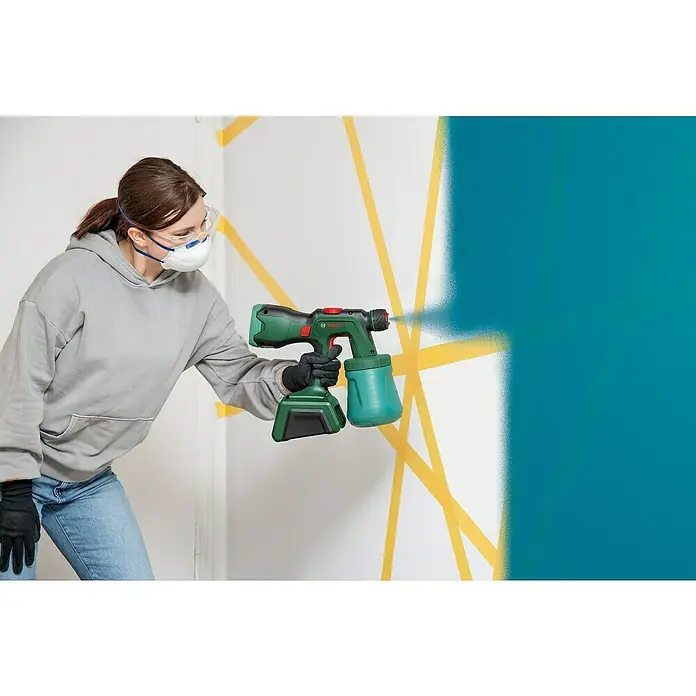 Bosch Power for All 18V Akku-Farbsprühsystem Universal Spray 18V-300 - 18 V, Ohne Akku, Max. Fördermenge: 0,3 l/min - Frau benutzt Bosch Farbsprühsystem, um eine Wand blau zu streichen, geschützt mit Maske und Brille.
