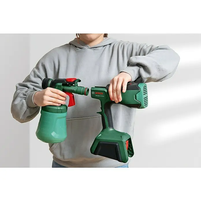 Bosch Power for All 18V Akku-Farbsprühsystem Universal Spray 18V-300 - 18 V, Ohne Akku, Max. Fördermenge: 0,3 l/min - Eine Person hält eine grüne Bosch UniversalSpray 18V-300 Farbspritzpistole mit Akku und Tank.