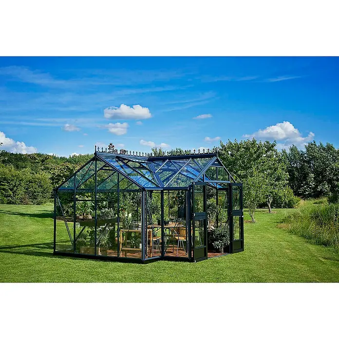 Juliana Gewächshaus Orangerie - Außenmaß inkl. Dachüberstand (B x T): 439 x 373 cm, Material Seitenwand: Glas, 3 mm, Anthrazit/Schwarz - Geräumiges Gewächshaus mit Pflanzen und Tisch mit Stühlen im Grünen. Die Tür des Gewächshauses ist geöffnet.