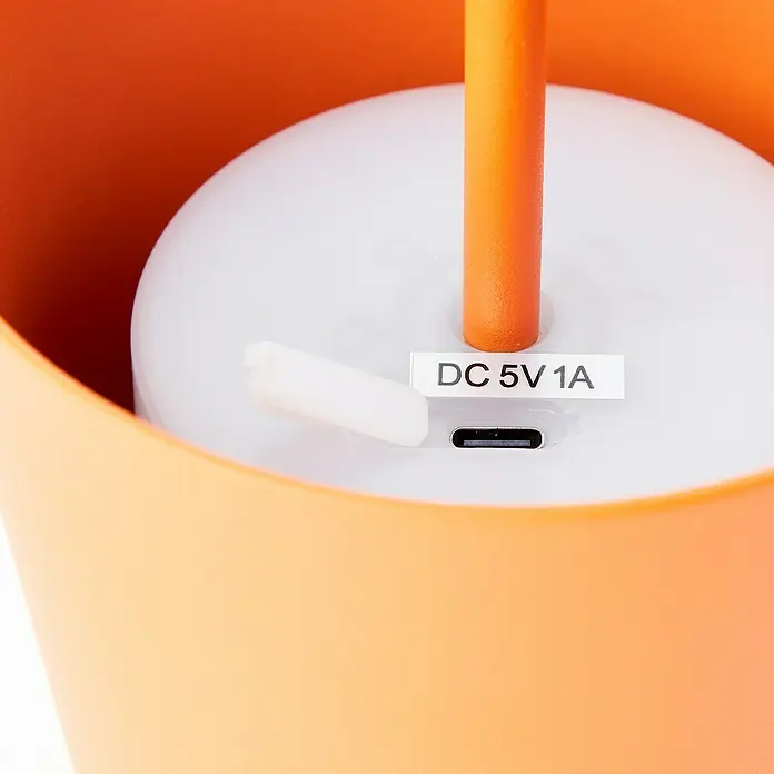 Brilliant Akku-Tischleuchte Kaami - 2 W, Orange, Warmweiß - Detailansicht einer orangefarbenen Lampe mit USB-Anschluss und dem Aufdruck "DC 5V 1A" für die Stromversorgung.