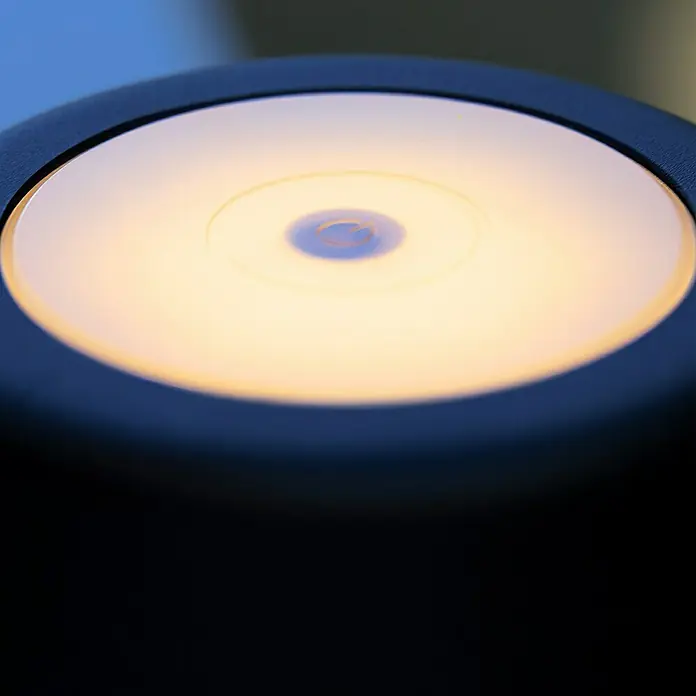 Brilliant Akku-Tischleuchte Kaami - 2 W, Schwarz, Warmweiß - Nahaufnahme einer runden, warm leuchtenden LED-Lampe in einem dunklen Gehäuse. Ideal für stimmungsvolle Beleuchtung.
