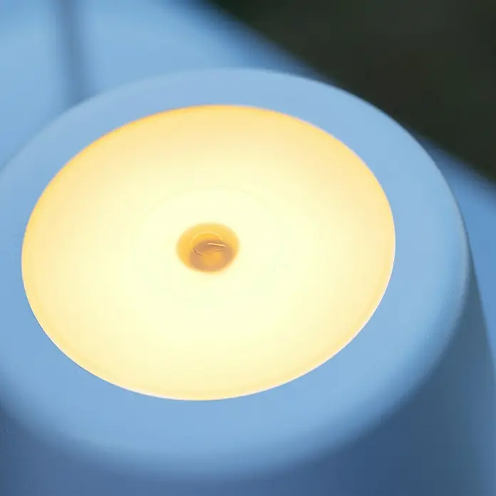 Brilliant Akku-Tischleuchte Kaami - 2 W, Weiß, Warmweiß - Nahaufnahme einer runden, blauen Lampe mit warmem, gelbem Licht, die eine gemütliche Atmosphäre schafft.