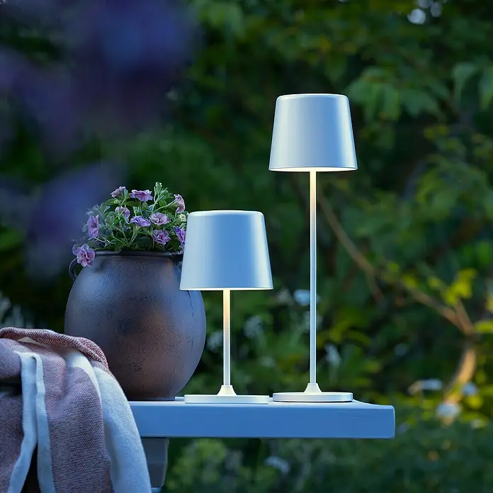 Brilliant Akku-Tischleuchte Kaami - 2 W, Weiß, Warmweiß - Zwei weiße LED-Tischleuchten unterschiedlicher Höhe auf einem Tisch im Freien, die ein warmes Licht ausstrahlen.