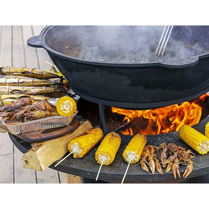 Purline Barbacoa de carbón EFP57B - Diámetro de la superficie de la parrilla: 60 cm, Negro - Un gran caldero negro sobre un fuego abierto, rodeado de mazorcas de maíz, cangrejos de río y pescado ahumado para un festín delicioso.